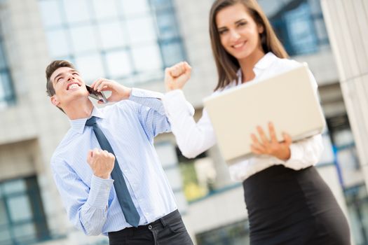 Young business couple standing in front of office buildings caught in the moment of joy for the successful completion of the job.