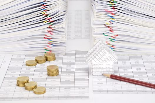 House and pencil with step pile of gold coins on finance account have dual pile overload document of report with colorful paperclip as background.