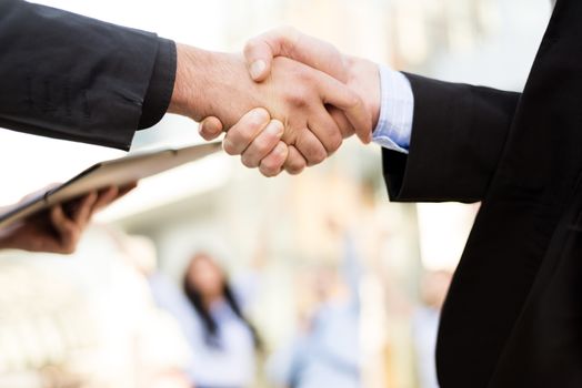 Hands of two business men shaking hands in the background can be seen by business people and office building.