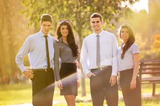 Small group of business people, elegantly dressed, standing in the park, looking at the camera, enjoying the sunny day.