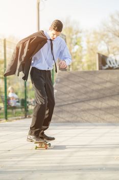 Young businessman, elegantly dressed, holding a jacket draped over shoulder standing on a skateboard.