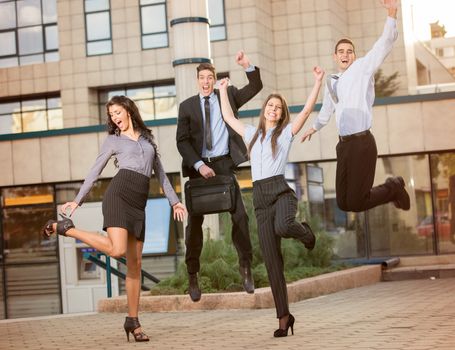 Group of young business people jumping in front of the company celebrating a successful job.