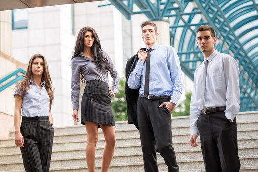 Group of young business people, elegantly dressed, standing on the steps of the company's building.