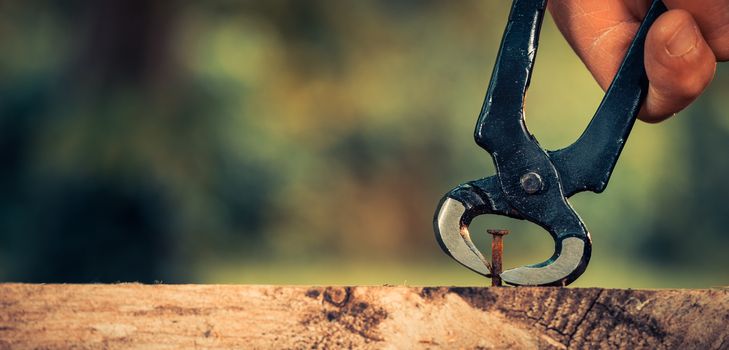 Pulling a carpenter tip on wood with pliers outdoor