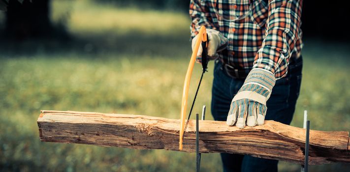 Senior man sawing a log handsaw closeup