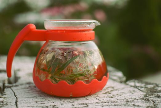 teapot of fruit tea with herbs and berry on the white tree stump.