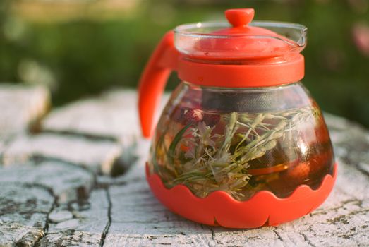 teapot of fruit tea with herbs and berry on the white tree stump.