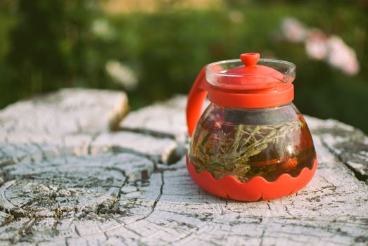 teapot of fruit tea with herbs and berry on the white tree stump.