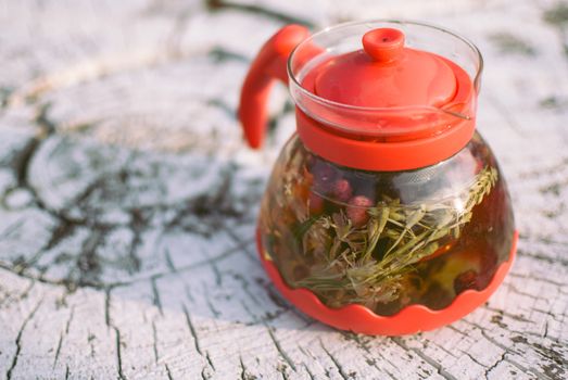 teapot of fruit tea with herbs and berry on the white tree stump.