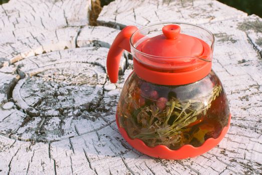 teapot of fruit tea with herbs and berry on the white tree stump.