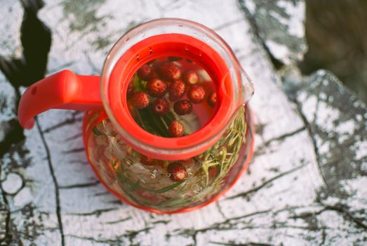 teapot of fruit tea with herbs and berry on the white tree stump. top view