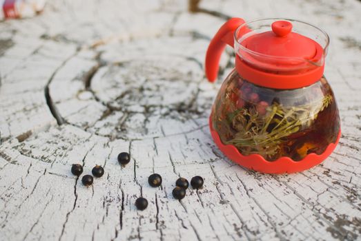 teapot of fruit tea with herbs and blackcurrant berry on the white tree stump.