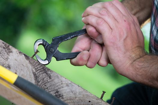 Pulling a carpenter tip on wood with pliers outdoor