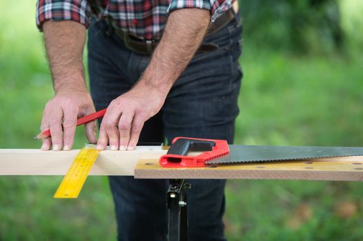 Carpenter sawing a wooden square with a wood saw outdoor