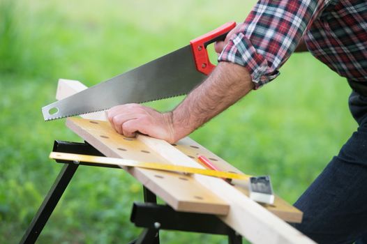 Carpenter sawing a wooden square with a wood saw outdoor