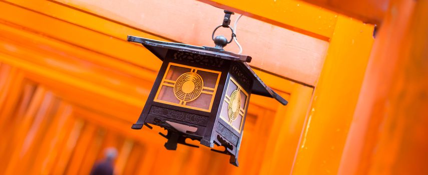 Red Tori Gate at Fushimi Inari Shrine in Kyoto, Japan. Selective focus on traditional japanese lamp. Panoramic composition.