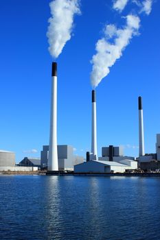 Factory chimneys at energy plant with blue sky and lake