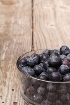 Clear glass bowl of ripe blueberries on a rustic farm picnic table in summer.