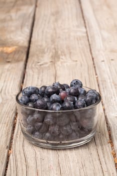 Clear glass bowl of ripe blueberries on a rustic farm picnic table in summer.