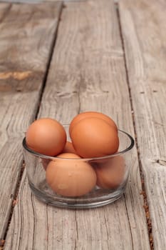 Fresh organic brown eggs in a clear glass bowl on a rustic farm picnic table in summer.