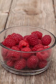 Clear glass bowl of ripe raspberries on a rustic farm picnic table in summer.