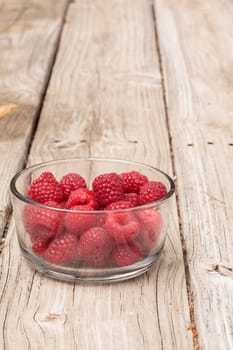 Clear glass bowl of ripe raspberries on a rustic farm picnic table in summer.