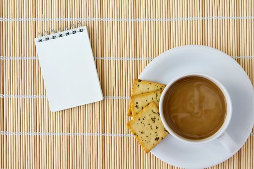 White cup of hot coffee and white sketch book on a mat 