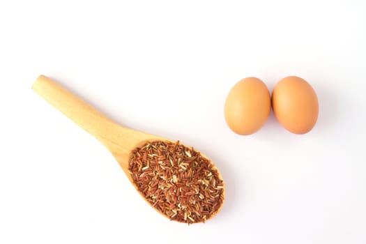 Brown egg and wooden spoon with red rice; on a white background