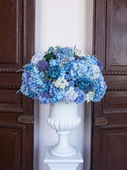 Flower arrangement of colorful summer blooms in a white pottery in front of the wooden door and white wall