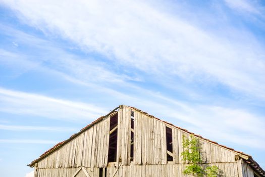 Roof of an old broken barn, blue sky with clouds