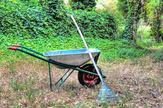 hdr of wheelbarrow in a garden and a rake