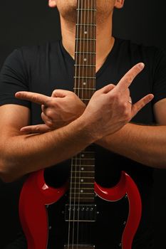 Man holding embracing red sg guitar neck with two hands showing devil horns rock metal sign over black background