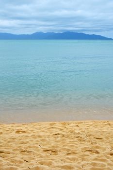 Footprints on sand beach shore over blue sea and cloudy sky background 