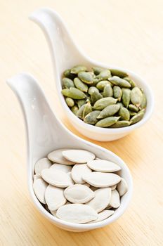 Peeled pumpkin seeds in white spoon on wooden background.