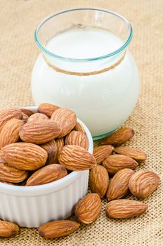 Almond and almond milk in glass on sack background.