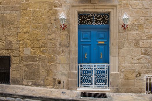 Bright blue door - entrance to an old stone house. Decorative lanterns with the maltese cross base. Seglea, island Malta.