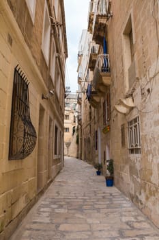 All the old stone buildings in the light orange color with small windows and balconies. Senglea, mediterranean island Malta.