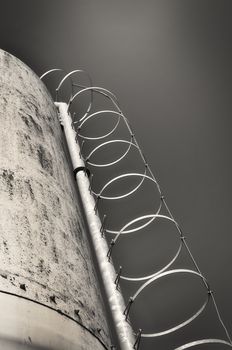 A round ladder climbing a silo in concrete, monochromatic.