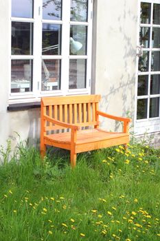 Orange bench on grass with window and lamp in background