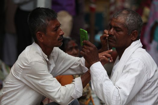Pune, India  - ‎July 11, ‎2015:A streetside barber shaves a pilgrim during a huge pilgrimmage in India