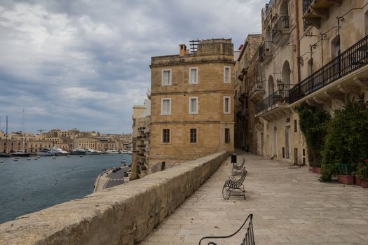 Old stone houses on the banks of the mediterranean sea. Benches to enjoy the view on the port. Cloudy sky.