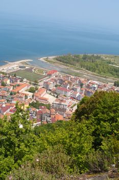 General top view of Ayancik town in Sinop in Black Sea region inside green trees with blue sea, on bright sky background.