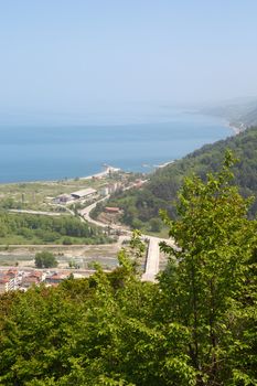 General top view of Ayancik town in Sinop in Black Sea region inside green trees with blue sea, on bright sky background.
