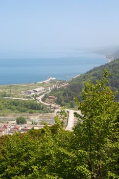 General top view of Ayancik town in Sinop in Black Sea region inside green trees with blue sea, on bright sky background.