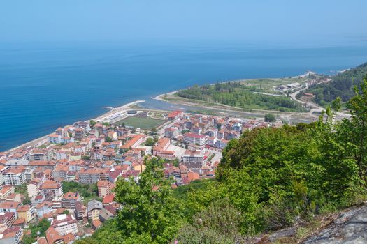 General top view of Ayancik town in Sinop in Black Sea region inside green trees with blue sea, on bright sky background.