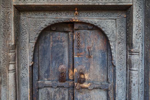 Close up front view of wooden old door, closed with chains and locked with padlock.