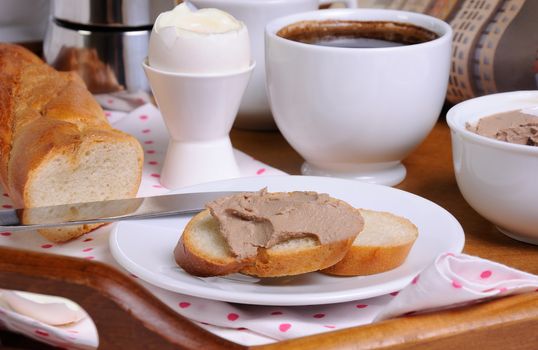 A slice of toast spread with liver pate for breakfast and a cup of coffee on a tray
