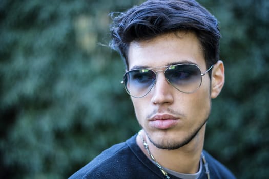 Headshot of handsome young man in city street, looking to a side, wearing sunglasses