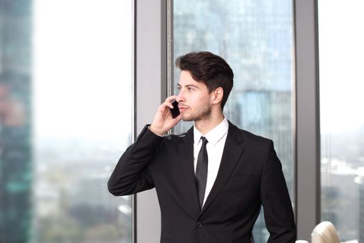 Businessman with cellphone working in office with view at skyscrapers