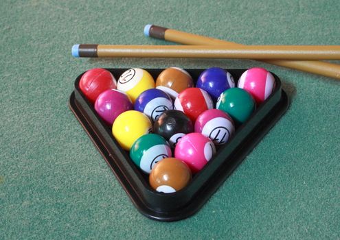 Pool balls on green cloth in triangle with cues